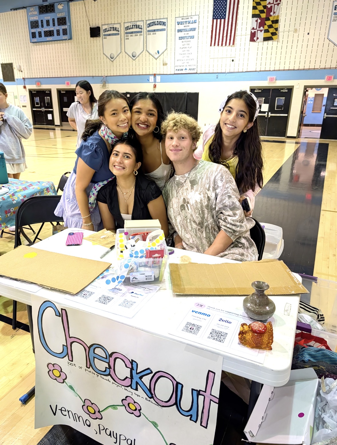A few volunteers smiling behind the Project Sewing Hope checkout table