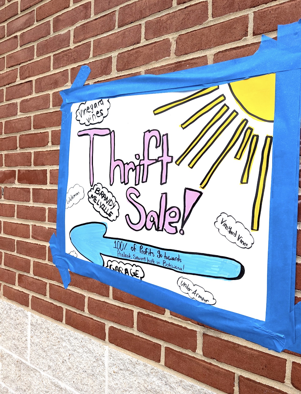A handmade thrift sale sign taped to a brick wall
