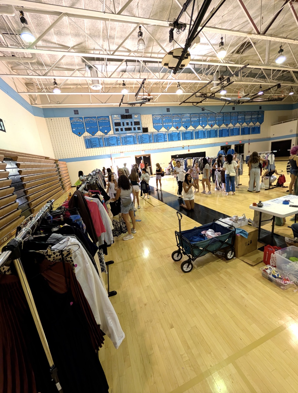 A bright gym filled with clothing racks and shoppers at the Project Sewing Hope thrift sale