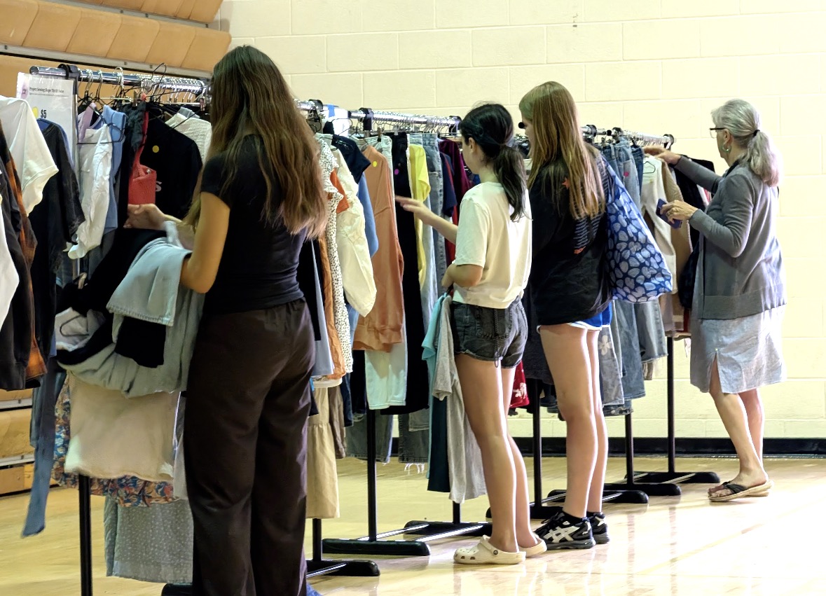 Shoppers browsing a long row of clothing racks at the thrift sale