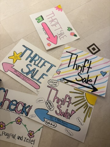 Several colorful handmade thrift sale and checkout signs on the floor